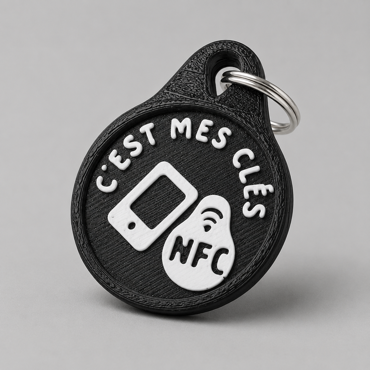 Round black plastic NFC keychain with white text reading c'est mes clés and an NFC icon on a metal ring.