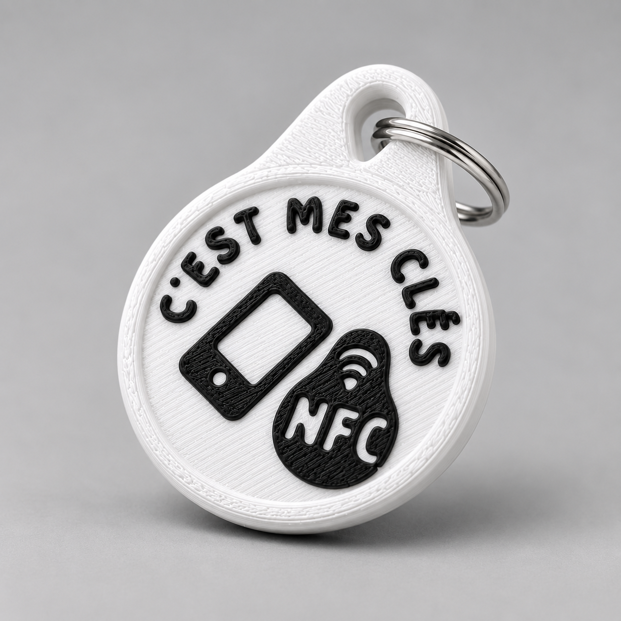 Round white plastic NFC keychain with black raised text reading c'est mes clés and an NFC icon on a metal ring.